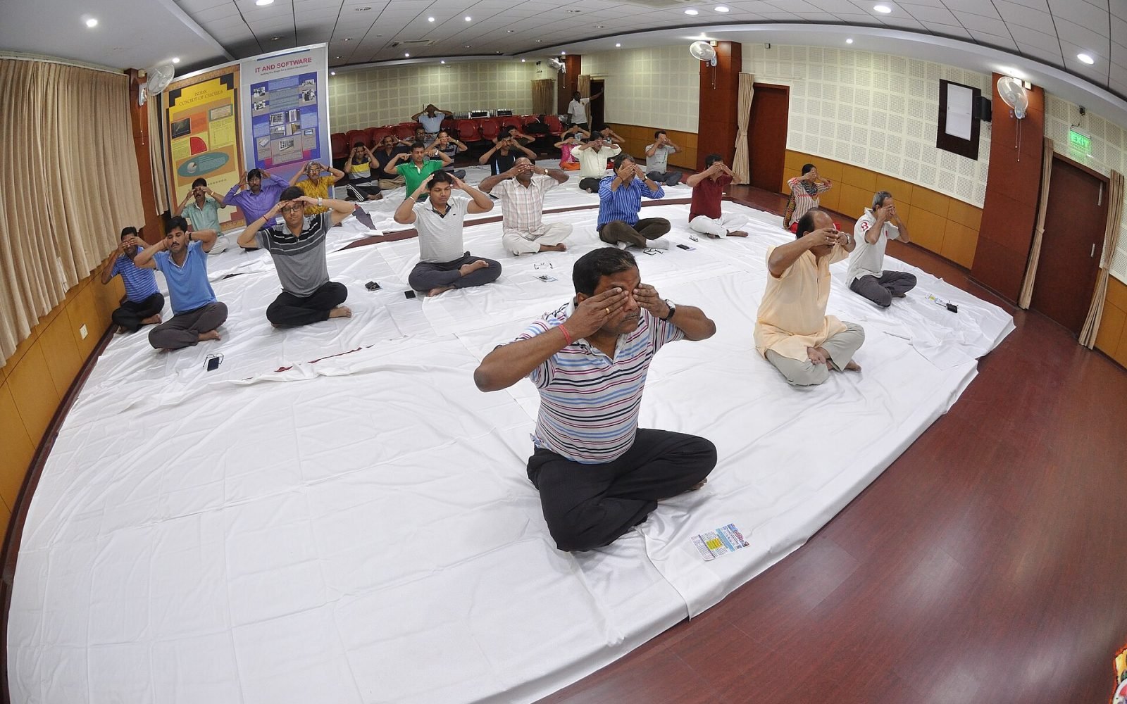 Two students practise nadi shodhana, alternate-nostril breathing, seated outdoors on a lawn.